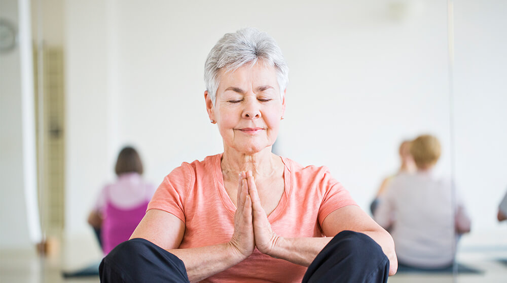 Senior woman in yoga class does peaceful sitting zen pose
