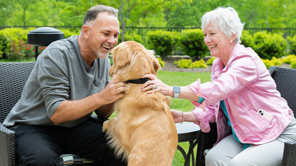 Tribute community members laugh and pet golden retriever in outdoor patio chairs