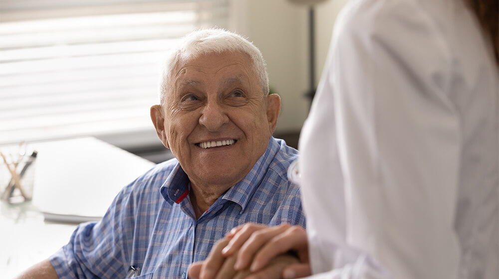 Man wears big smile while in doctors office and holds hands with physician