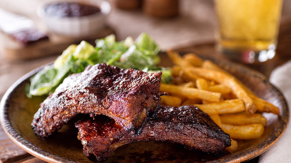 Plate of BBQ ribs with salad and fries next to glass of iced tea