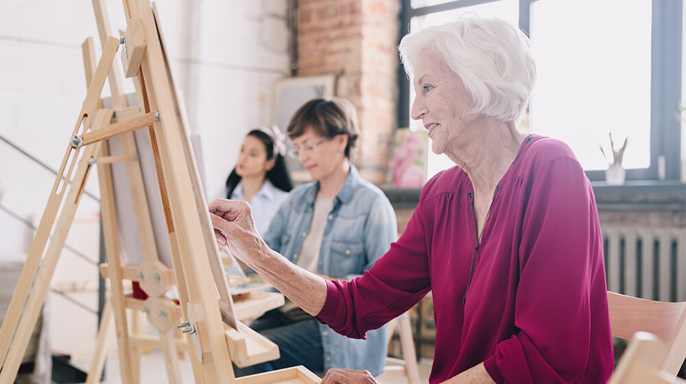 Group of women at different ages participate in an art class in an elevated, sunny loft