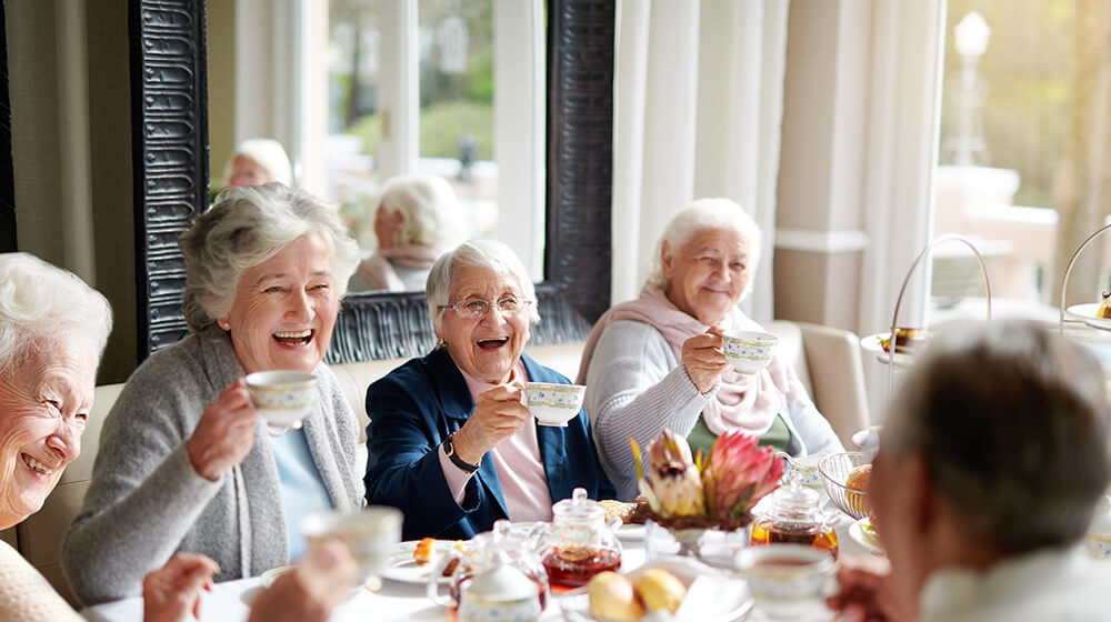 Laughing friend group all hold up cheers at tea time