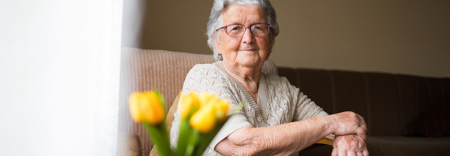 elderly white woman sitting behind yellow flowers