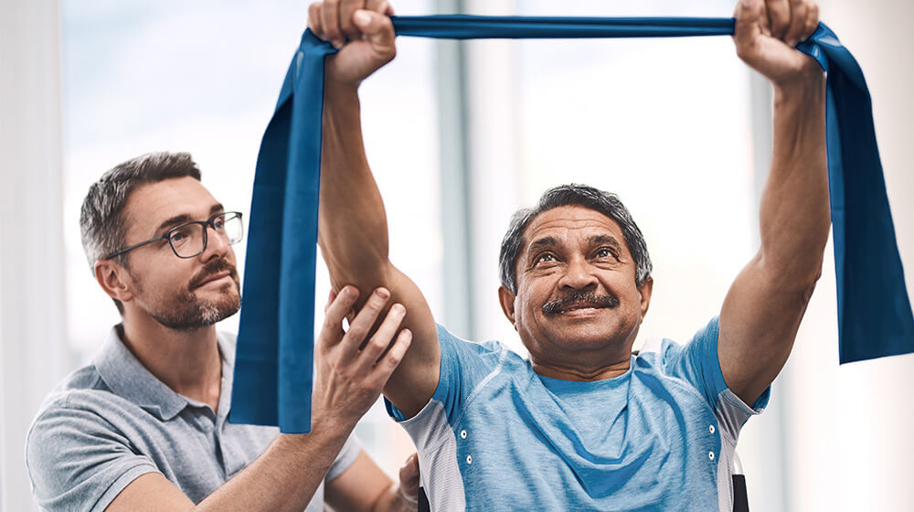 Older man works with younger staff member with stretching bands