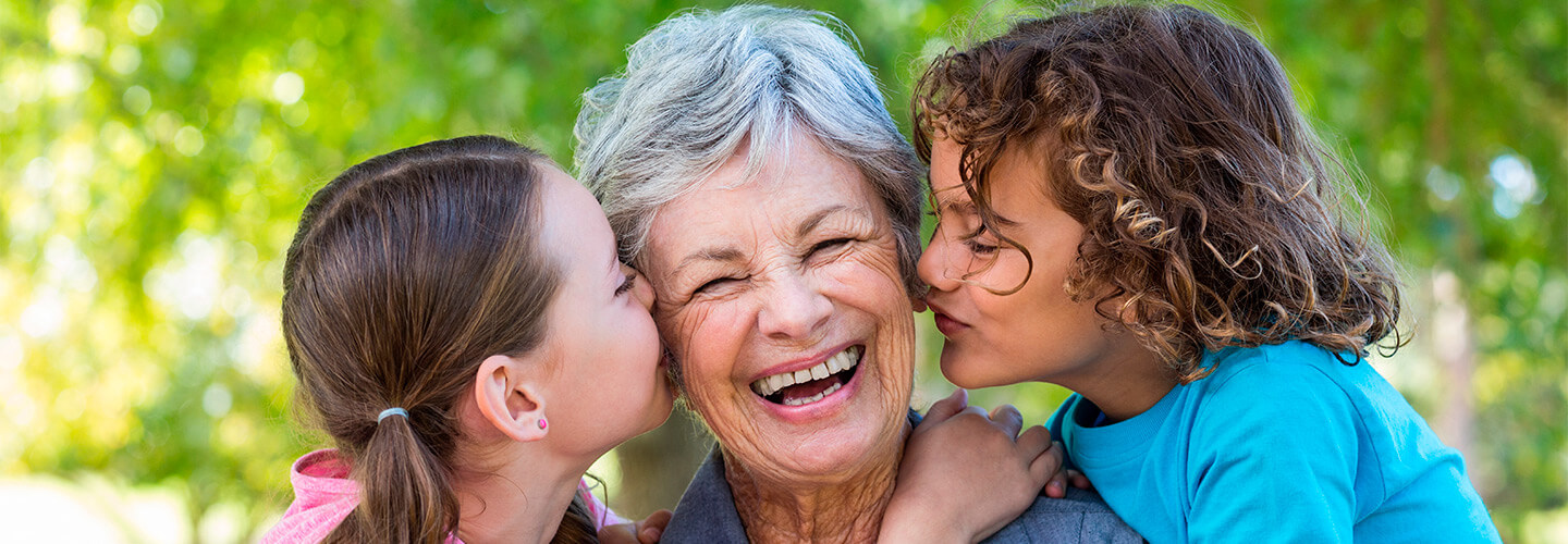 Grandmother laughs as her grandkids give her hugs and kisses outdoors
