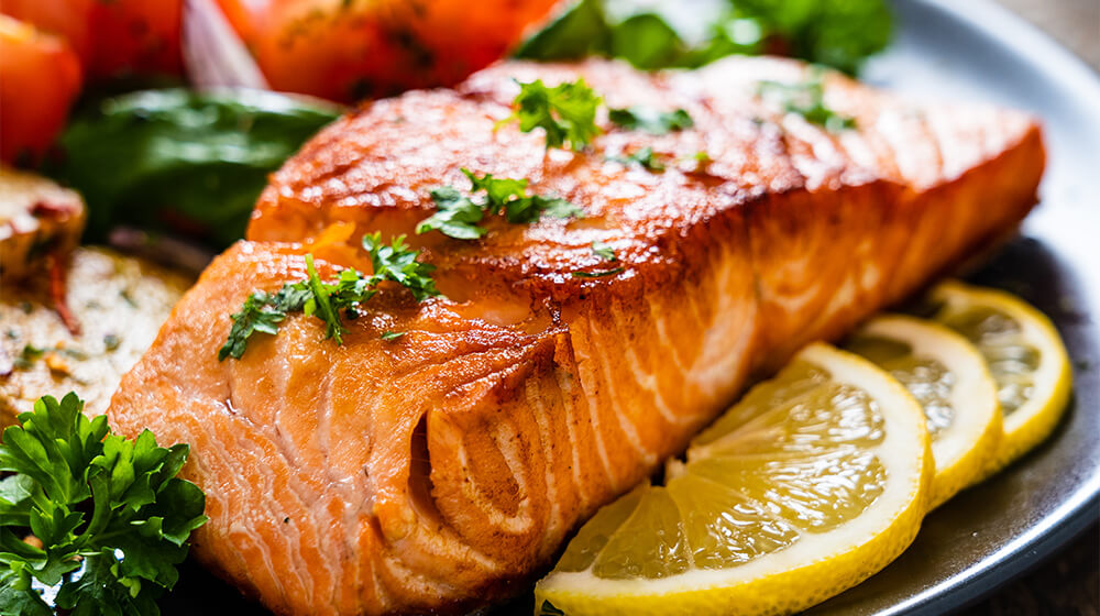 Barbecued salmon, fried potatoes and vegetables on wooden background
