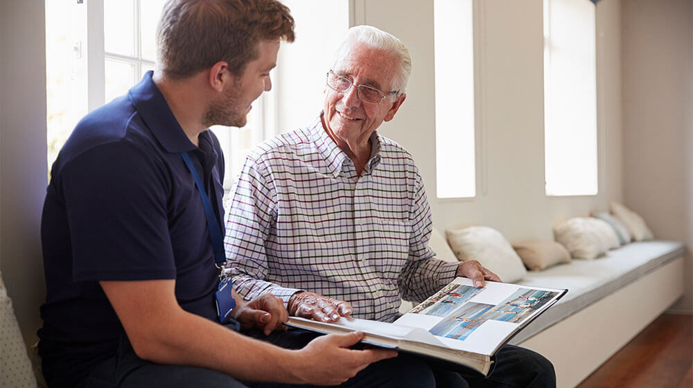 Senior man sitting looking at photo album with male nurse